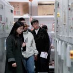 Visitors reviewing pellet plant electrical control cabinets with manufacturing staff