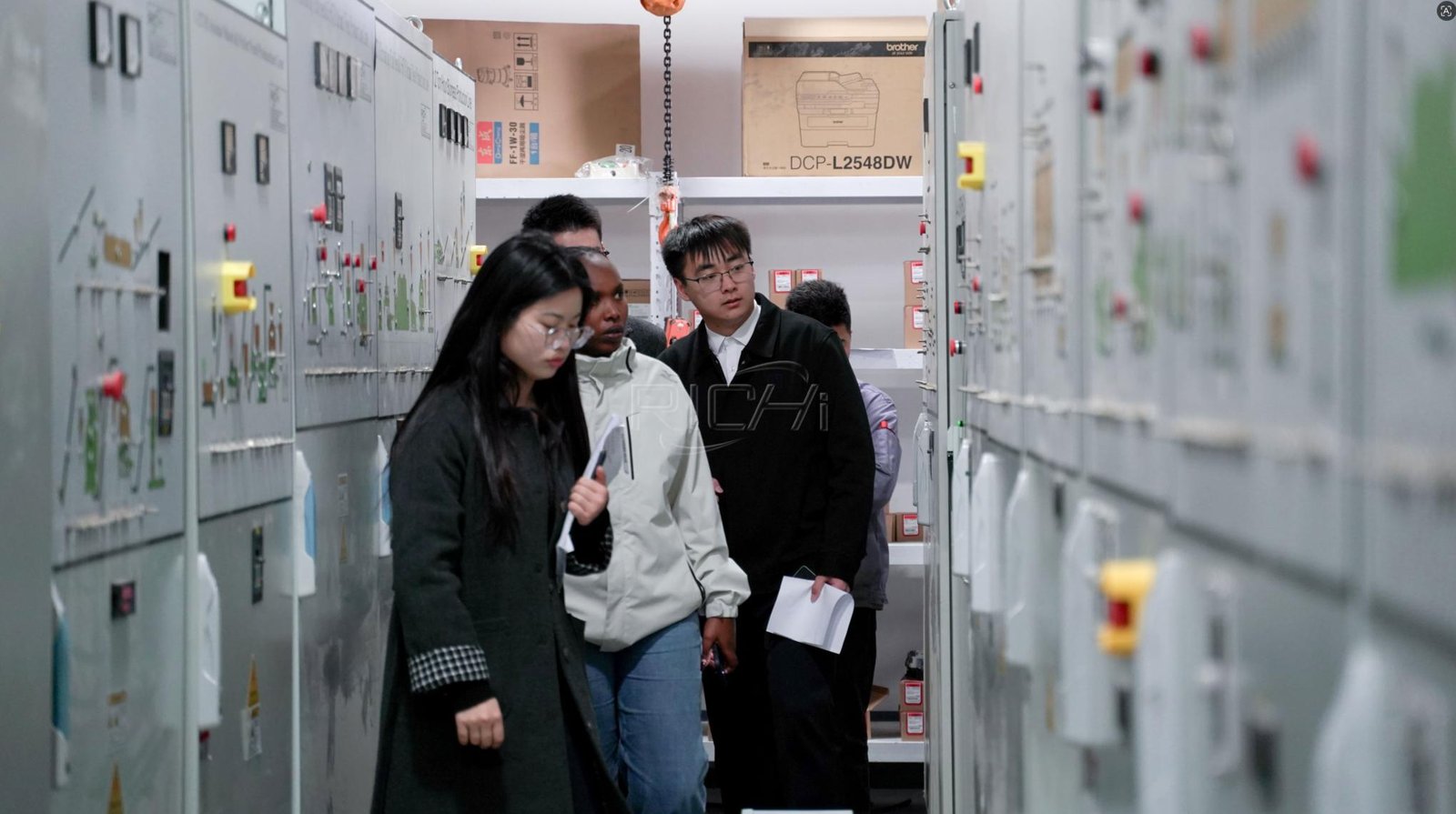 Visitors reviewing pellet plant electrical control cabinets with manufacturing staff